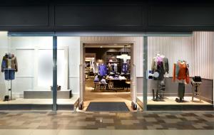 The entrance to a clothes store. It has mannequins and a large mirror displaying clothes and accessories. The floor is wooden inside and tiled outside, with the Esteem Ribbed II entrance mat laid in the doorway.