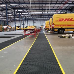 Yellow DHL vans back onto a walkway fitted with the Air Grid anti fatigue mat. The mat is black with a yellow safety border.