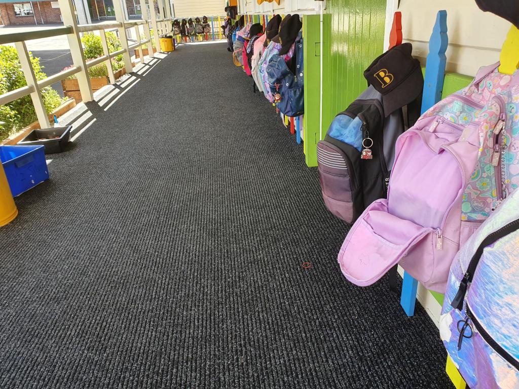 Children's bags are hung on pegs along an empty corridor. On the floor is the Dura Rub heavy duty entrance mat.