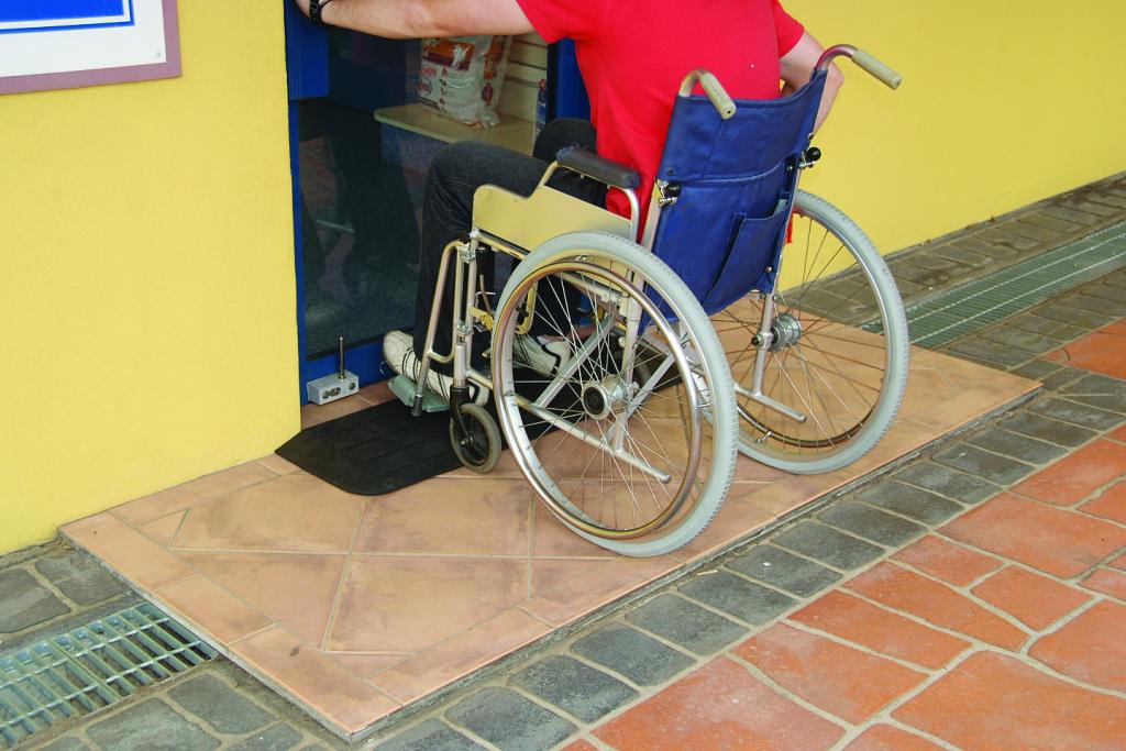A man wheels a wheelchair over an access ramp.