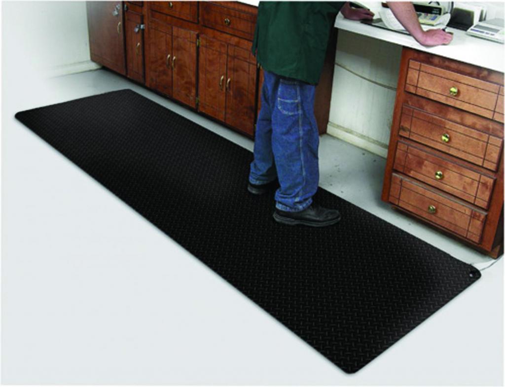 the diamond foot anti fatigue mat is laid under a mans feet as he works at a bench with draws either side