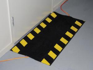 the cable safe mat is laid over a trailing wire. it has a yellow and black striped safety border to provide extra protection.