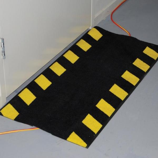 the cable safe mat is laid over a trailing wire. it has a yellow and black striped safety border to provide extra protection.