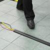 A cable protector is laid on a pavement over 3 wires. A person is bout to step over the wires safely thanks to the cable protector.