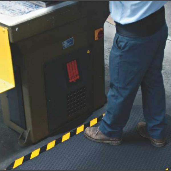 a man stands on the dura step weldsafe. It is laid in front of a large machine and is black with a yellow and black striped safety border.