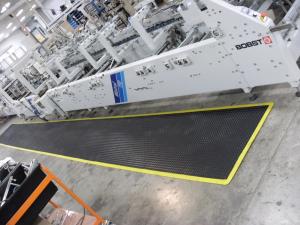 The ergo tread anti fatigue mat is laid in front of a BOBST machine. The machine is grey with dials and switches along the front. The mat is black with a yellow safety border.