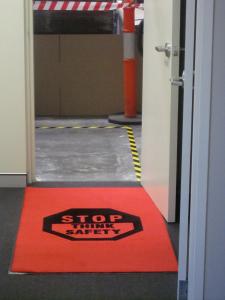 a red safety mat with black writing and a stop sign is placed on the floor at the door to a factory.