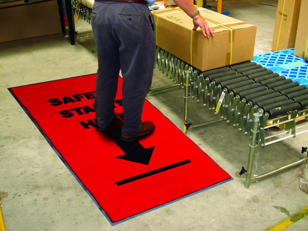 a man stands on a safety mat while seeing to a package on a conveyer belt.