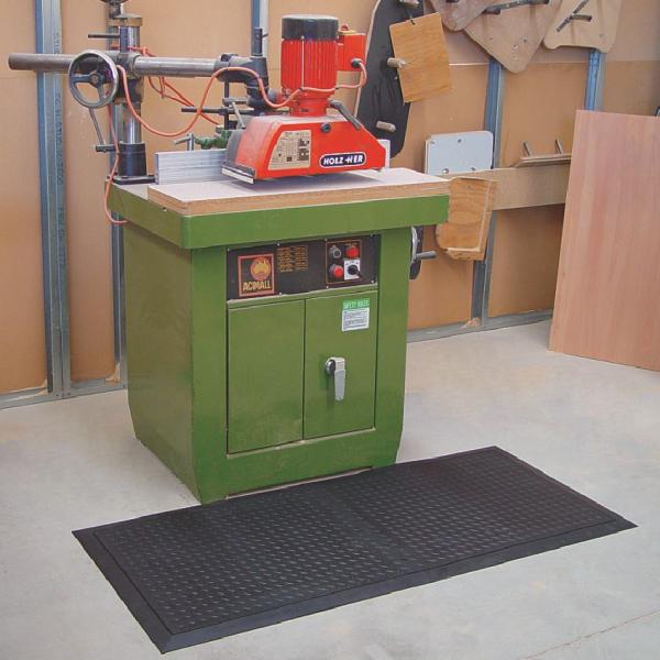 A green machine sits in a workshop. In front of it a black solid top anti fatigue mat is laid.