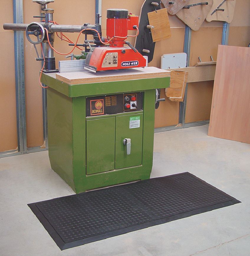 A green machine sits in a workshop. In front of it a black solid top anti fatigue mat is laid.