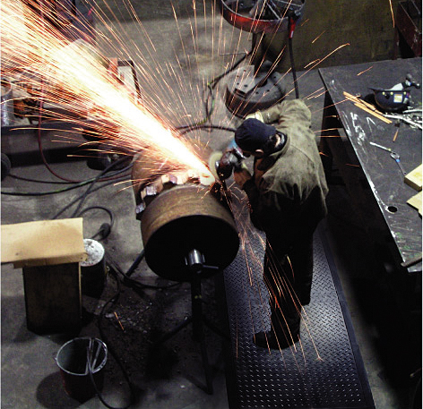 a welder creates sparks while wearing safety gear and standing on a welding safety mat