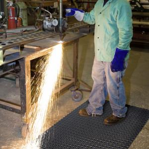 a welder stands on a fire resistant mat while working. Sparks are flying off the machine he is using but the mat is not catching alight.