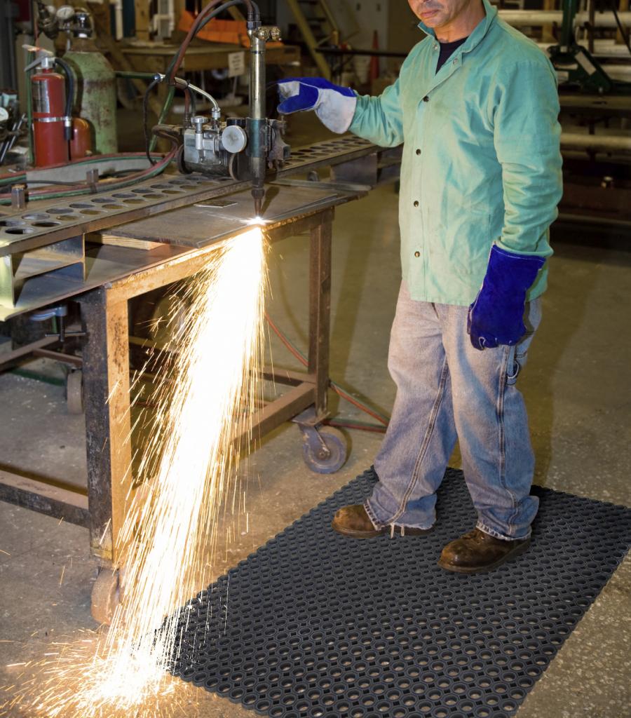 a welder stands on a fire resistant mat while working. Sparks are flying off the machine he is using but the mat is not catching alight.