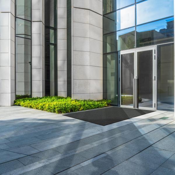 The opti-scrape is laid outside a glass door to a fancy office building. The floor is stone slabs and the walls are smooth white brick.