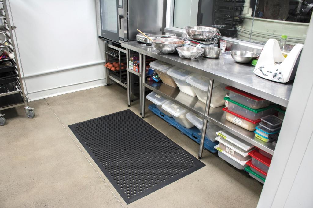 the cushion ease anti fatigue non slip mat is laid in a busy commercial kitchen. The mat is black with holes for drainage.