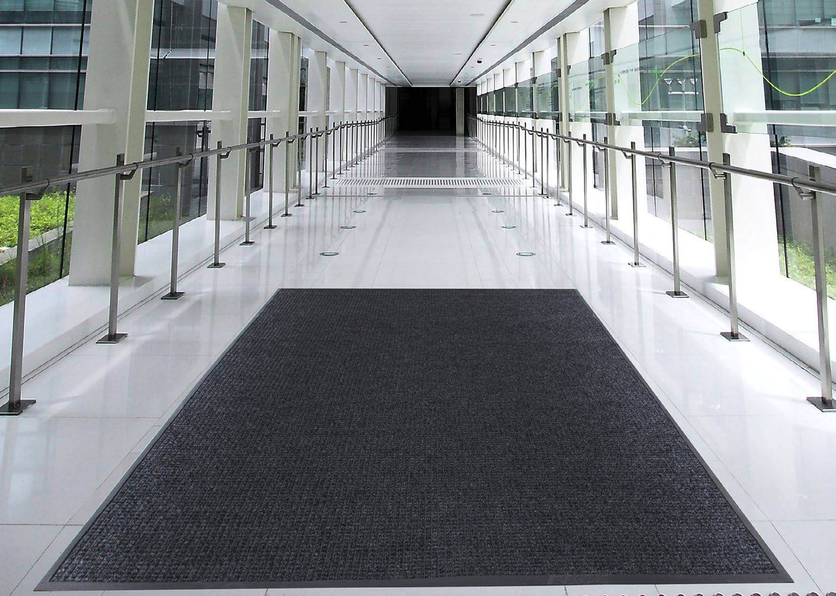 A black entrance mat is laid in a glass corridor with rails either side.