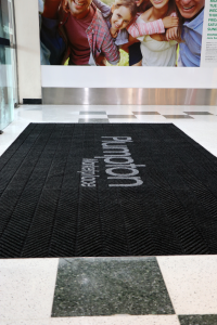 a stock family photo is on the wall inside the entrance to a shopping centre. On the floor, laid into a mat recess is the premium scraper entrance mat.