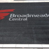 A black indoor entrance mat - the Premium Scraper - is printed with the logo for Broadmeadows Central shopping centre. The floor underneath the mat is white tiles.