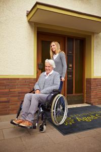 The Logo Mat Inkjet Plus is printed with the branding for a residential aged care home. A smiling lady pushes an elderly lady I na wheelchair over the mat.