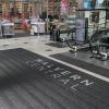 Malvern Central is printed onto the premium scraper logo entrance mat. Behind it, a shop selling bedding is seen and a couple travel up an escalator just in front.