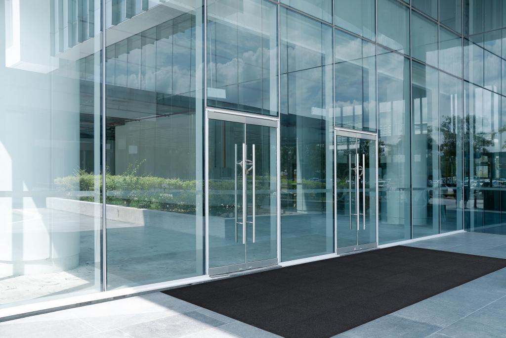 Outside a smart glass entranceway is a tiled floor topped with a modular entrance mat. The tiles interlock to form one large entrance mat.