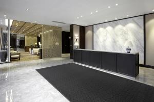 The Glamour Step entrance mat is laid in the reception area of a hotel. The reception has marbled white walls and floors with a black counter, and a lobby with sofas can be seen in the background.