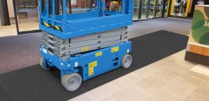 A scissor lift runs over a black floor mat in a large entranceway.