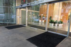 A smart looking entrance way with the address 350 Queen Street above the door. The doors are glass sliding and there are two entrance mats at either side. There is also a central door with a pull handle with no mat. A long black entrance mat runs along the inside of the doorway and some large indoor potted plants are in the background.