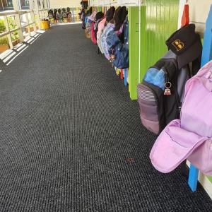 Children's bags are on pegs along an empty corridor. On the floor is the Dura Rub heavy duty entrance mat.