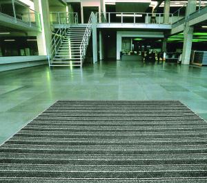 A green-tinged image of a commercial entrance fitted with the Master Scraper entrance mat. The mat is black and grey horizontal striped with raised strips in a lighter colour.