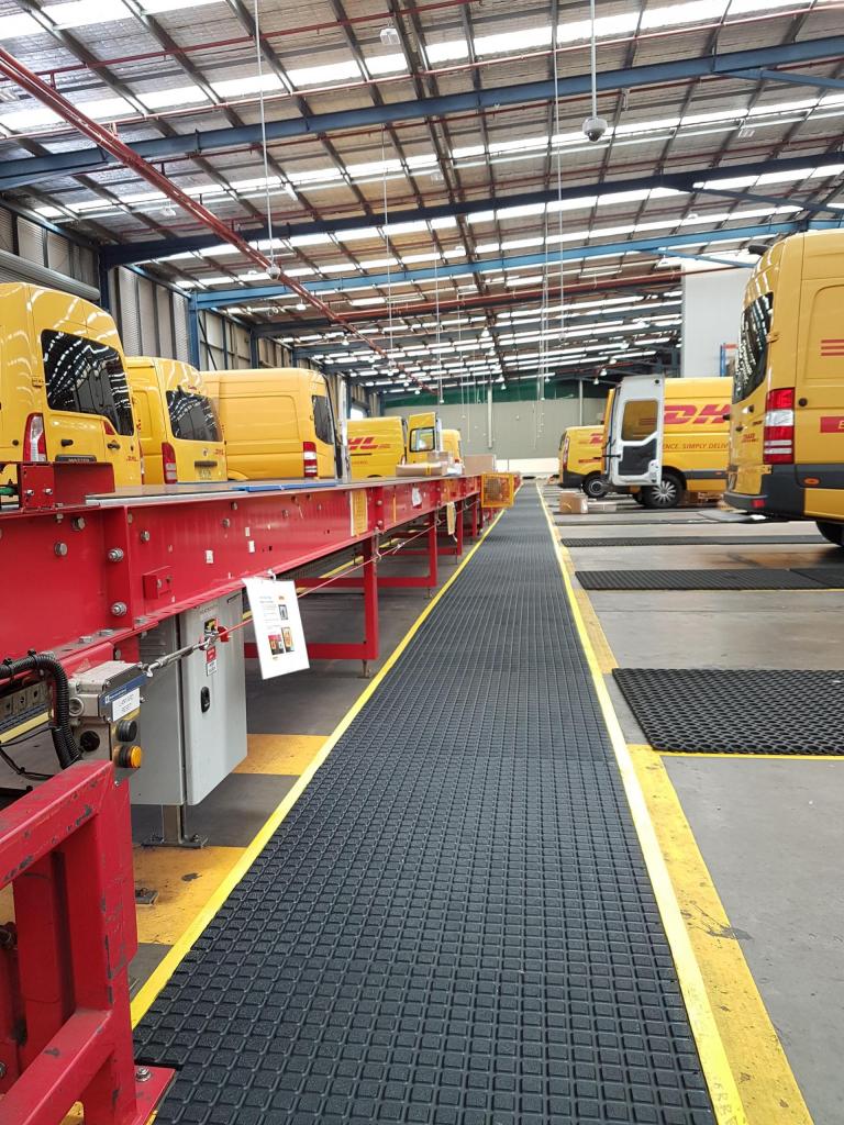 The Air Grid anti fatigue and non slip mat runs between two rows of yellow DHL vans that back onto a walkway