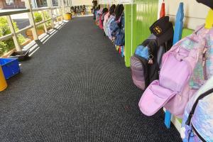 A close up of children's bags on pegs. On the floor is the Dura Rub heavy duty entrance mat.