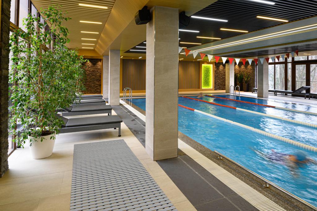 Indoor swimming pool area featuring lounge chairs, modern décor, and a safety mat placed along the poolside walkway. The setting highlights a clean, stylish, and safe environment for swimmers and guests.