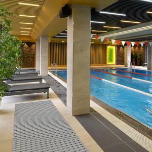 Indoor swimming pool area featuring lounge chairs, modern décor, and a safety mat placed along the poolside walkway. The setting highlights a clean, stylish, and safe environment for swimmers and guests.