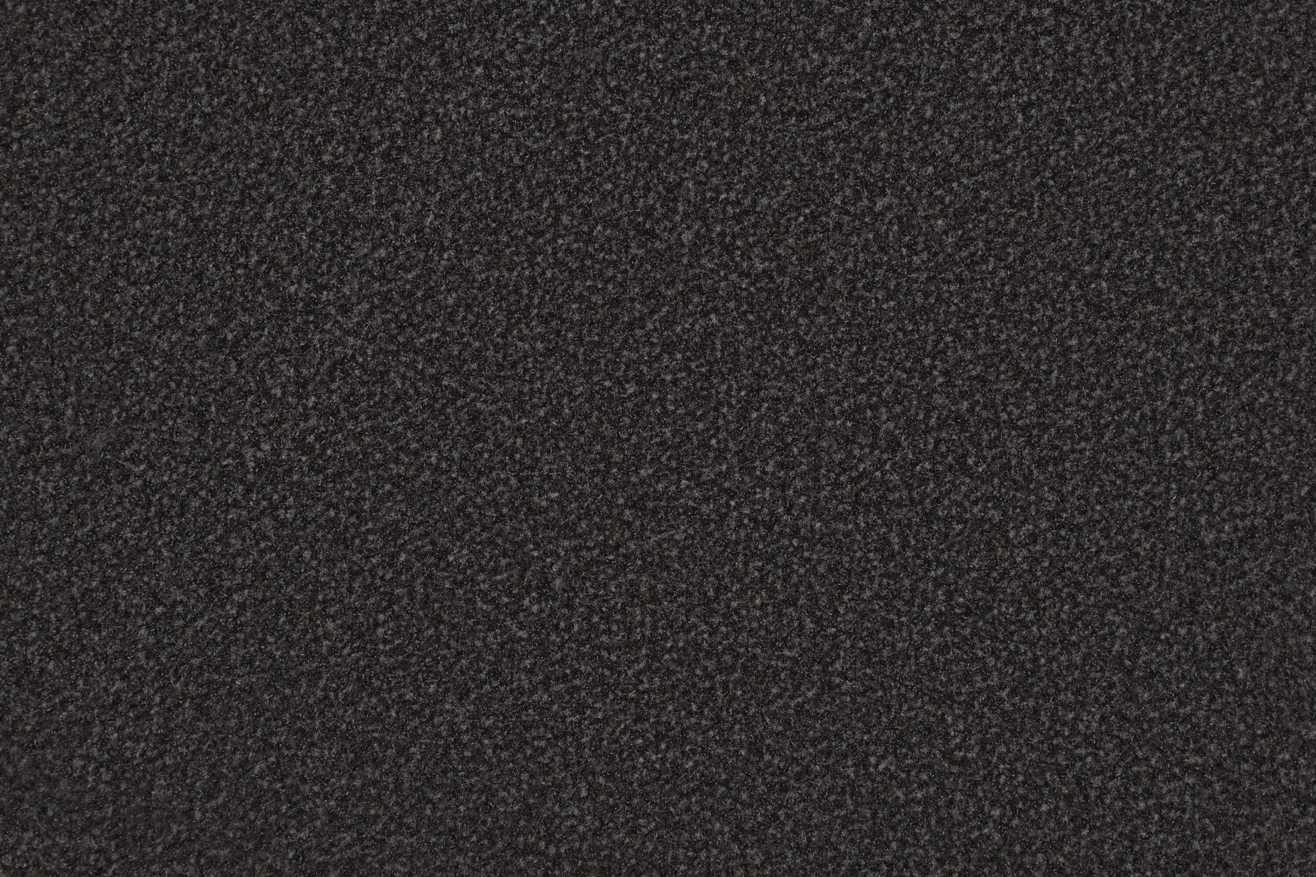 A close-up view of a dark, textured surface, likely a dense, rough carpet or floor mat material. The fibers appear tightly packed, creating a uniform, slightly speckled pattern across the entire image.